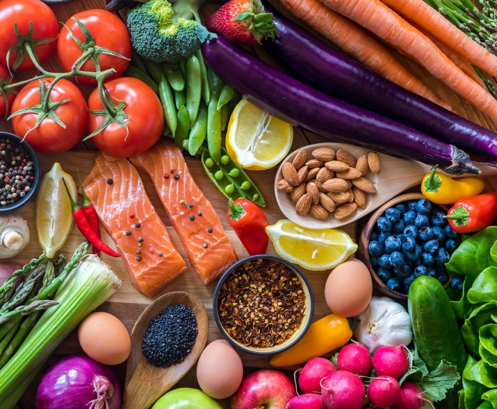 Frische Zutaten von oben: Lachs, Tomaten, Auberginen, Beeren, Nüsse, Eier, Radieschen und Salat auf einem Holzbrett
