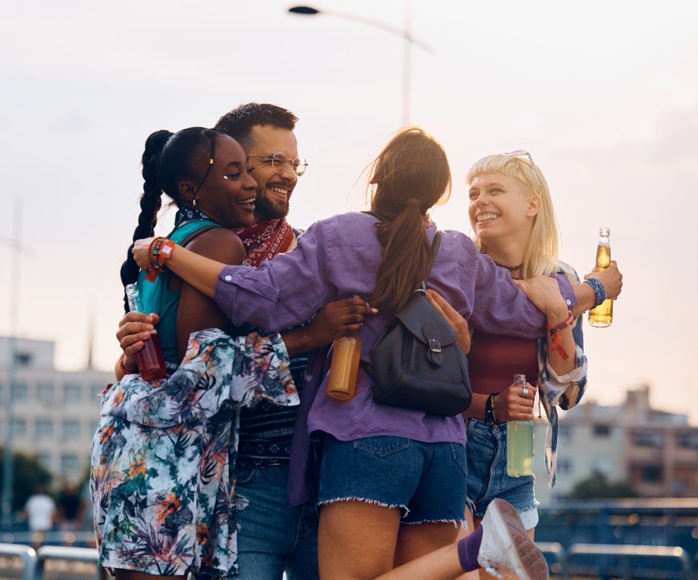 Vier lachende Freunde umarmen sich im Abendlicht im Freien
